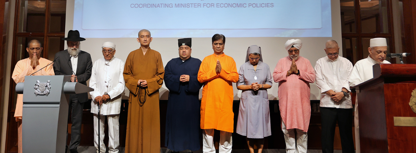 Group of 10 diverse religious leaders in robes standing together, hands clasped. One at podium.